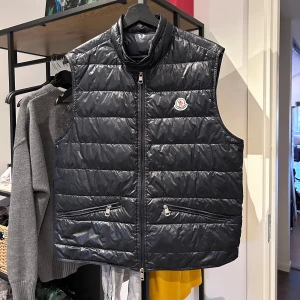 Moncler Gui Väst - Moncler Gui, skick 6/10 lagning längst ner på baksidan och 3 pinholes. En bak uppe till höger på västen (bild 2 syns knappt) en fram på bröstet (bild 5) och en fram längst ner (bild 4) Size 2-S/M, Navy, 8400 nypris. Skriv vid frågor/bilder,Pris satt!