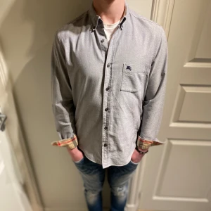 Burberry skjorta - Hej! Säljer nu dessa sjukt feta burberry skjortan. Den är självklart äkta (dessutom äkhetskontrollerad) Skjortan är i fint skick, inte använd särskilt mycket. Storlek M men kan passa S. Jag på bilden är 185cm. Färgen är blå/grå. Hör av er, allt gott🙌
