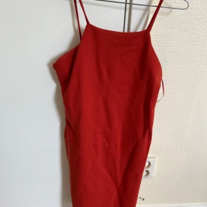 Röd klänning med tunna axelband - En röd klänning med tunna axelband. Klänningen har en enkel och elegant design, perfekt för sommarens festligheter.