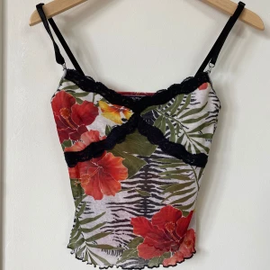 Blommig linnetopp från Jennyfer - En färgglad linnetopp från Jennyfer med ett blommigt mönster i rött, gult och grönt. Toppen har svarta spetsdetaljer och justerbara axelband. Den är tillverkad i ett lätt och bekvämt material.