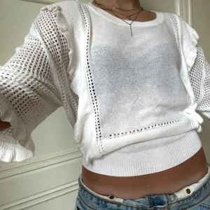 Trekvartsärmad stickad tröja. - Vit stickad tröja med volanger och kortare ärmar. Den är luftig och funkar till alla årstider!