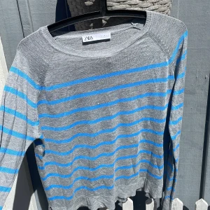 Grå och blå randig tröja från Zara - En bekväm grå tröja från Zara med blå ränder. Tröjan har långa ärmar och en rund halsringning. Perfekt för vardagsbruk.