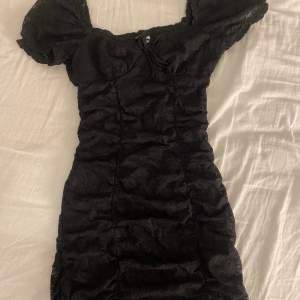 Ganska kort svart klänning som är figursydd och sitter fint på kroppen, blommigt mönster och puffiga ärmar, använd 1 gång