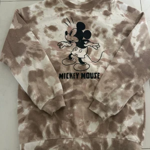 Tjocktröja  - Det är en beige/brun tjocktröja med en svart mussepigg på