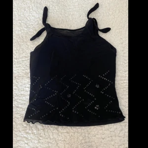 Söt svart topp med paljetter! - En söt svart topp med dubbeltyg, knutbara snören i ärmarna och paljetter på framsidan! 