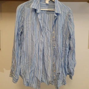 Blå randig skjorta  - Blå randig skjorta i mjukt glänsande tyg med vita ränder. Coola detaljer i placeringen av knapparna! Inte så stretchig vilket gör den perfekt till jobb eller fest beroende på styling! 💙 Lite skrynklig men ingen match för en steamer 😉