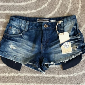 Lågmidjade shorts med slitningar - Assnygga shorts med slitningar som är helt oanvända med lappen kvar men säljer då de är för stora. De är i strl 34 men skulle säga att de mer är som 36!! Använd köp nu och skriv om du har några frågor❤️