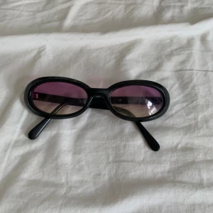 Svarta solglasögon med lila linser - Ett par svarta solglasögon med ovala lila linser. Glasögonen har en modern design med breda skalmar och en bekväm passform. (ai har skrivit lol)