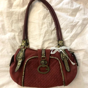 Röd väska med guldiga detaljer  - En fin röd väska med guldiga detaljer, helt ärligt så vet jag inte var den är ifrån då jag köpte den här på plick. Tycker att den är fin men har svårt att göra outfits med den pågrund färgen, skriv till mig om ni undrar om något mer 💕🫶