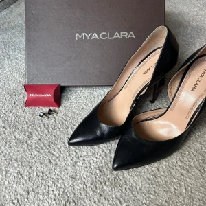 Svarta pumps från Mya Clara - Eleganta svarta pumps från Mya Clara med spetsig tå och hög klack. Skorna är tillverkade i skinn och har en stilren design. De är i använda en gång, men sulan är smutsig. det tillhör extra klackar (se bild). Köparen står för frakt! 11 cm klack 