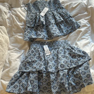 Blåmönstrad topp och kjol-set från Ginatricot - Säljer ett superfint set från Ginatrocot med smockad topp med tunna axelband och volang, samt matchande kjol med volang. Båda i blått och vitt mönster, perfekt för sommardagar. Sval bomullskvalitet och snygg passform.