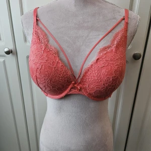 Hunkemöller korallfärgad bh, storlek 75D - Korallfärgad bh med spetsdetaljer och dekorativa band framtill som man kan ta bort. Dock är färgen på bilderna starkare . Använd 2 ggr . Nypris 599 kr