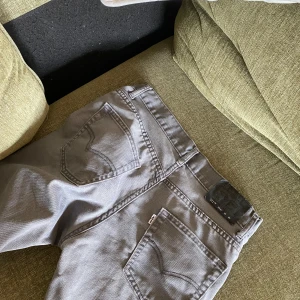 Grå jeansbyxor från Levi's - Säljer ett par grå jeansbyxor från Levi's med klassisk femficksdesign och knappgylf. Byxorna har raka ben och normal passform, perfekt för en avslappnad stil. Slim fit 29/30