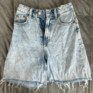 Ljusblå jeansshorts från Divided H&M - Säljer ett par ljusblå jeansshorts från Divided H&M. De har fransiga benslut, klassisk femficksdesign och knapp- samt dragkedjestängning. Perfekta för sommaren och ger en avslappnad look.