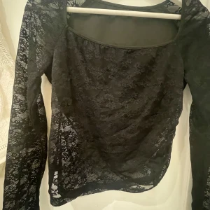 Svart spetsblus med långa ärmar - Säljer en svart blus i genombruten spets med långa ärmar och rundad halsringning. Perfekt för dig som gillar en elegant och trendig stil. Tunn och lätt, passar bra att styla lager på lager. Inbyggt tyg som är thkande över bröstet och ryggen