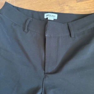 Svarta kostymbyxor från Madlady - Säljer ett par svarta kostymbyxor från Madlady i storlek EU34. Byxorna har hällor för bälte och klassisk rak passform. Perfekta till många olika outfits och enkla att matcha. Passar mig som vanligtvis har 36