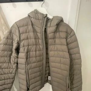 Beige pufferjacka från Strova - Säljer en beige pufferjacka från Strova i storlek M. Jackan har huva, dragkedja framtill och quiltad design. Perfekt för kyliga dagar och enkel att matcha med olika outfits.