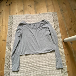 Grå croppad långärmad tröja från 157 - Säljer en enkel och stilren grå croppad långärmad tröja från 157. Tröjan är tillverkad i en mjuk bomullsblandning med viskos och elastan, vilket gör den bekväm och stretchig. Perfekt till jeans eller kjol. Naken är väldigt öppen