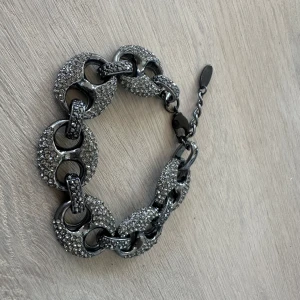 Glittrigt armband med stora länkar - Säljer ett snyggt armband med stora, runda länkar i mörk silverfärg. Länkarna är täckta av glittrande stenar som ger ett lyxigt intryck. Perfekt accessoar för att lyfta din outfit!