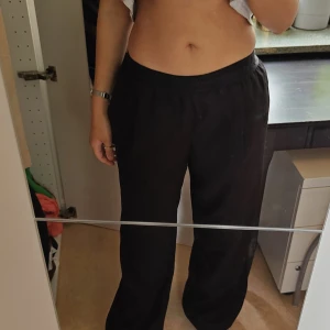 CW Svarta vida byxor med resårmidja - Säljer ett par svarta byxor med breda ben och resår i midja från Carin Wester CW. Byxorna har en avslappnad passform och är perfekta för en chill och bekväm stil. Materialet känns mjukt och lätt, vilket gör dem sköna att bära hela dagen. Behöver en rejäl omgång med klädroller!