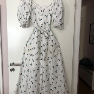 Vit blommig långklänning med puffärmar från DAY - Superfin vit långklänning med blått blommönster och puffärmar. Klänningen har markerad midja med knytband samt en vit underklänning. Perfekt för vår och sommar👗☀️🌸🌼. Nypris 2200kr. Använd gärna köp nu🌟.