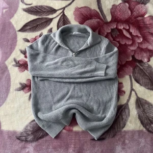 Grå stickad tröja med dragkedja från Zara - Säljer en stilren grå stickad tröja från Zara med halv dragkedja och hög krage. Tröjan har lång ärm och ribbade muddar, perfekt för lager-på-lager. Enkel att matcha och passar till många tillfällen. Nästan aldrig använd