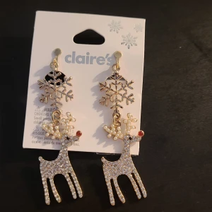 Glittriga renörhängen från Claire's, clipons - Superfina örhängen från Claire's med glittriga renar och snöflingor i guld. Renarna är dekorerade med små pärlor och stenar, och har en röd detalj på nosen. Perfekta för vintern och julens alla tillfällen!