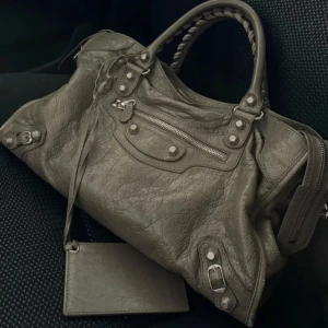 Grå handväska med dragkedja och detaljer - Säljer en grå handväska med klassisk design och silverfärgade metalldetaljer. Den är sliten vid handtaget och därav priset❤️