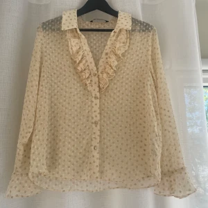 Beige blus med volang och prickigt mönster - Säljer en söt blus med volang längs knäppningen och krage.