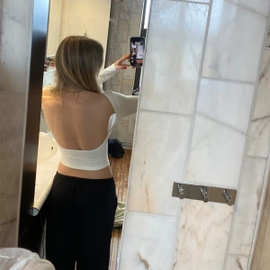Vit långärmad topp med öppen rygg - Säljer en vit långärmad topp med polokrage och öppen rygg. Toppen är tight och har en stilren design som passar perfekt till olika outfits. Materialet ser ut att vara mjukt och stretchigt.