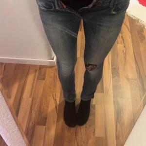 Blå jeansbyxor med patch från Miss Sixty - Säljer ett par blå jeansbyxor från Miss Sixty med skinny passform och låg midja. Byxorna har en unik patch med motiv på ena benet och snygga slitningar. Klassisk femficksmodell och dekorativ knapp framtill.                               Vet inte om det är miss sixty står air force på dom men ai skrev de.                            Mycket detaljer på insidan och utsidan