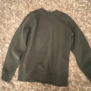 Mörkgrön sweatshirt från Weekday - En stilren mörkgrön sweatshirt från Weekday med rund halsringning och långa ärmar. Tröjan har en klassisk passform och är tillverkad i mjukt bomullsmaterial. Perfekt för en avslappnad och enkel look.
