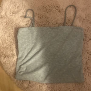 Grå croppad linnetopp från Gina Tricot - Säljer en enkel och stilren grå croppad linnetopp från Gina Tricot. Toppen har smala axelband och är perfekt för varma dagar eller som lager under andra plagg.