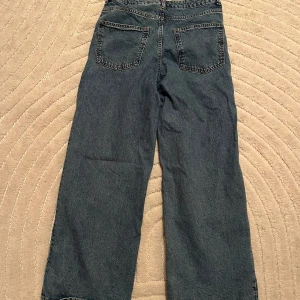 Blåa vida jeans med hög midja - Säljer ett par blåa jeans med hög midja och raka, vida ben. Klassisk femficksmodell med knapp och dragkedja framtill. Jeansen har en avslappnad passform och är perfekta för en trendig vardagslook. Kolla min profil för fler kläder!