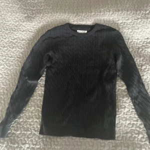 Svart kabelstickad tröja från Basic You - Svart kabelstickad tröja från Basic You i ekologisk bomull. Klassisk rund halsringning och långa ärmar. Perfekt för lager-på-lager och enkel att matcha med olika outfits.