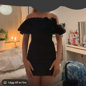 Svart klänning med volang - Säljer en svart klänning med stora volangdetaljer upptill. Klänningen är tight och har en axelbandslös design som ger en snygg och trendig look. Perfekt för dig som vill sticka ut med en elegant och stilren outfit. Storlek M men insydd så mer en S