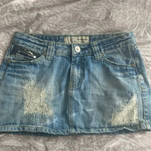 Jeanskjol  - Säljer en blå jeanskjol  med slitna detaljer och rhinestones. Några rhinestones på baksidan har lossnat tyvärr. Passar någon som har S i storlek🩵