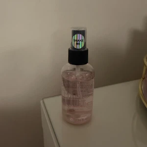 Rosa face mist med sprayfunktion - En rosa face mist i genomskinlig plastflaska med svart spraykork och etikett där det står 'SHAKE ME'. Perfekt för att fräscha upp huden under dagen och ge extra lyster.