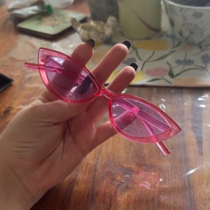Rosa cat eye-solglasögon - Säljer ett par trendiga solglasögon i cat eye-modell med transparent rosa bågar och matchande rosa glas. Perfekta för att ge din outfit en färgklick och en cool retrovibe.