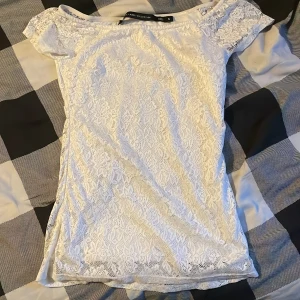 Vit spetsblus med kort ärm - Säljer en söt vit blus i spets med korta ärmar och rund halsringning. Blusen är figurnära och har ett romantiskt spetsmönster över hela plagget. Perfekt att styla till olika tillfällen!