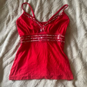 Röd paljett linne topp y2k - Säljer en jättesöt röd topp med smala axelband och dekorativa paljettdetaljer längs bysten och midjan. V-ringad och tajt upptill, babydoll topp passform typ. 