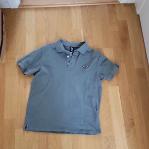 Grön piké t-shirt från Replay - Säljer en stilren grön piké t-shirt från Replay med klassisk krage och knappslå framtill. T-shirten har korta ärmar och en liten logotyp på bröstet. Perfekt för en avslappnad men snygg look.