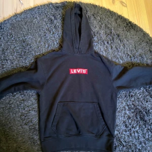 Svart hoodie från Levi's - Säljer en svart hoodie från Levi's med klassisk röd logga på bröstet. Tröjan har huva och en stor magficka framtill. Perfekt för en avslappnad och cool stil. Storlek S i bra skick dock inga band vid halsen se på bild 1