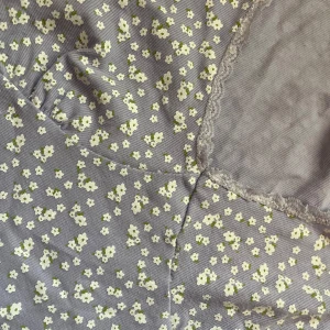 Ljuslila blommig croppad topp från Cotton On - Superfin ljuslila croppad topp från Cotton On med små vita blommor och v-ringning. Toppen har spetsdetaljer längs halsringningen och nederkanten samt korta ärmar. Perfekt för vår och sommar!