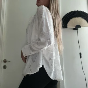 Off white skjorta från H&M - Säljer en vit skjorta från H&M med strukturerat tyg, som ny! Använd EN gång. Storlek M. Oversizad fit! Rundad nederkant!