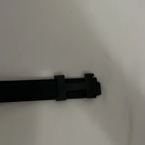Svart bälte med H-spänne - Säljer ett stilrent svart bälte med ett stort H-format spänne. Bältet är gjort i skinn och har en modern, minimalistisk design. Perfekt accessoar för att lyfta din outfit.