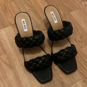 Svarta flätade klack-sandaler från NA-KD - Säljer ett par svarta sandaler med klack från NA-KD. Skorna har två breda, flätade remmar och fyrkantig tå. Perfekta för dig som vill ha en stilren och trendig look. Storlek 41