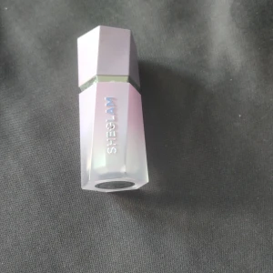 Chroma-Glow Bloom Liquid Highlighter Flying Comet - Säljer en flytande highlighter från Sheglam i nyansen Flying Comet. Förpackningen är sexkantig och skimrande lila med holografisk text. Perfekt för att ge ansiktet en strålande glow. 60 kr ny.