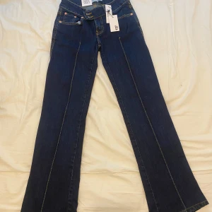 Mörkblå bootcut jeans från 157 - Säljer ett par mörkblå bootcut jeans från 157 med snygga kontrastsömmar och klassisk femficksdesign. Jeansen har låg midja och stängs med dragkedja och två knappar. Perfekta för dig som gillar en tidlös och trendig look. Ny pris: 400kr