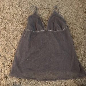 Grå mesh-linnetopp med spetsdetaljer - Säljer en grå linnetopp i mesh med tunna axelband och spetsdetaljer längs urringningen. Toppen har en liten rosett framtill och är lätt transparent, perfekt för lager-på-lager-stil.